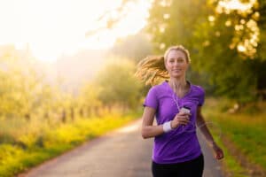 Woman listening to music on her earplugs and MP3 player while jogging along a country road in a healthy lifestyle
