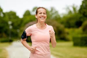Smiling Woman in 40s jogging with earphones wearing armband for smartphone