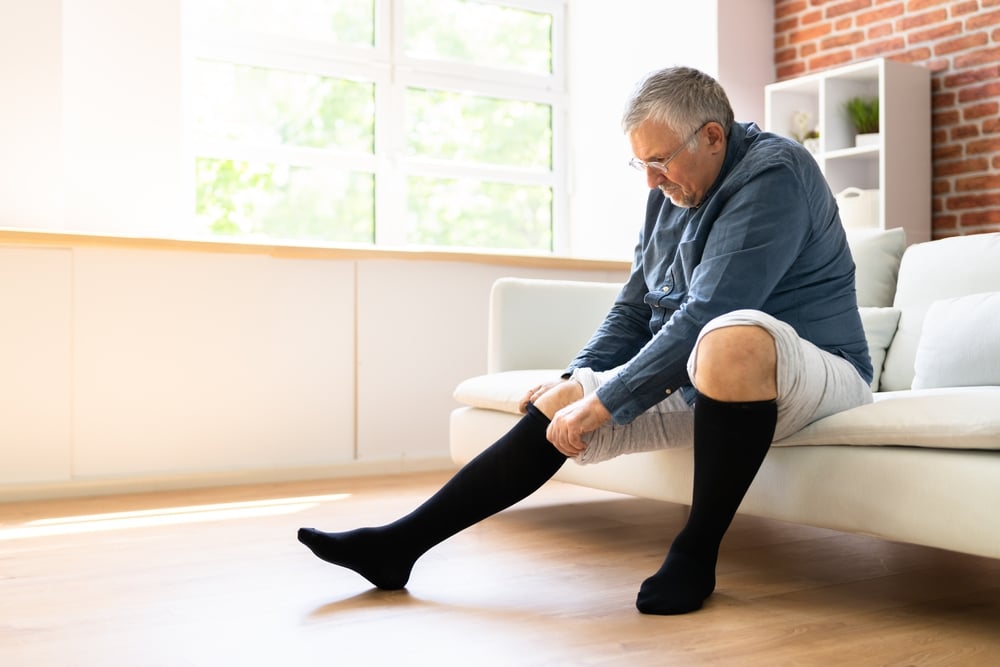 Older man putting on compression socks to help with his vascular health and circulation.